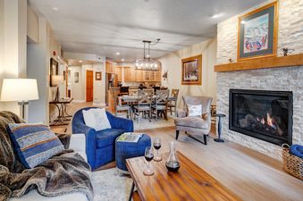 Cozy living room in Town Pointe A102 featuring a stone fireplace, plush seating, and an open layout into the dining and kitchen areas.