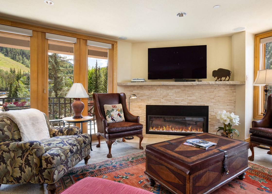 Cozy living room with a stone fireplace, leather armchairs, and scenic mountain views at 411 Beaver Creek Lodge.