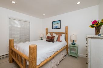 A cozy bedroom at River Street Refugio, featuring a rustic log bed with white bedding, patterned pillows, and a mountain painting above the headboard.