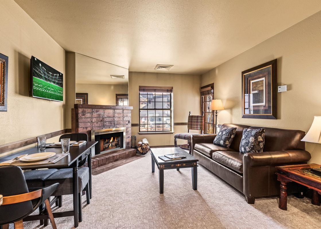 A comfortable and inviting living area inside Copperbottom Inn 101, featuring a lit fireplace, a dining table, a large leather sofa, and a television.