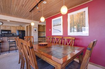 A detailed shot of the dining area in Chateau Chamonix CX133, showcasing a large wooden dining table with tiled inlays, surrounded by eight wooden chairs with X-backs.