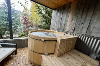 A private outdoor wooden barrel hot tub with bubbling water on a patio surrounded by trees at Magic on Main.