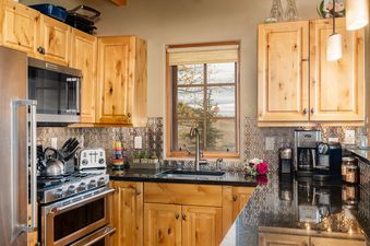 Moonlight Basin 3 Bandit Way kitchen features stainless steel appliances, a large window with a mountain view, wood cabinets, and a black granite countertop.