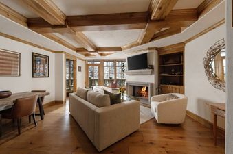The living area of Chateau Beaver Creek Residence 206 features a warm fireplace, a comfortable sofa, and large windows with a winter view.