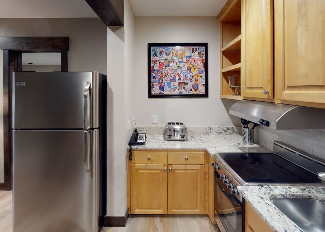 The kitchen in Manor Vail 165 features stainless steel appliances, granite countertops, a breakfast bar, and a full-sized refrigerator.