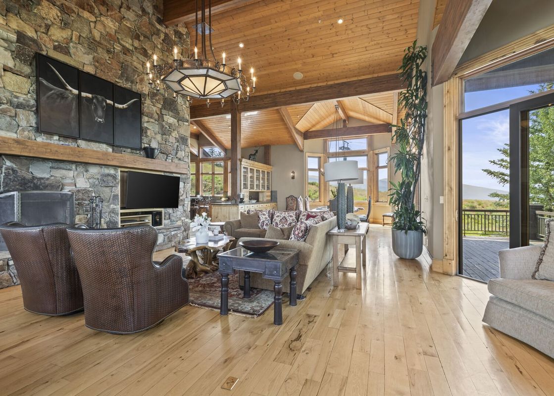A large living room with a stone fireplace and floor-to-ceiling windows offering a view of the mountains.