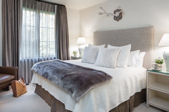 A sophisticated bedroom at Lodge at Shooting Star 04, featuring a bed with a grey upholstered headboard, white bedding, a faux fur throw, and bedside tables with lamps.