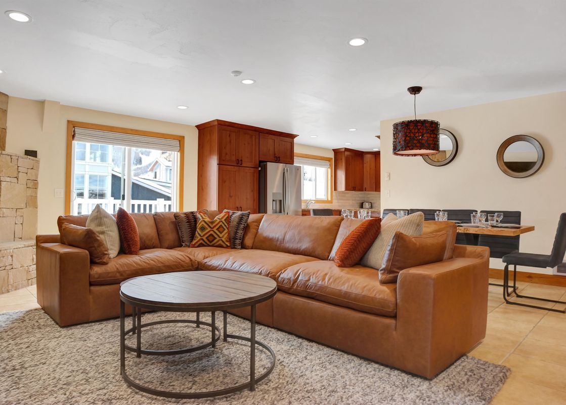 A spacious living room in Resort Plaza 5043 with a brown leather sectional, a round coffee table, and a view of the adjacent kitchen and dining area through a large window.