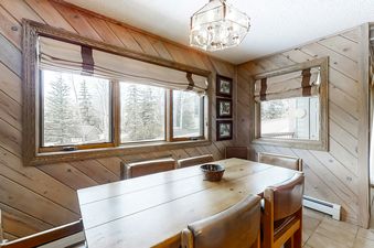 The dining area in Phoenix 215 features a long wooden table with multiple chairs and large windows offering views of the surrounding natural landscape.