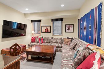 A cozy entertainment room at Webb Residence featuring an L-shaped sectional sofa with Southwestern patterns, a wooden coffee table, a wall-mounted TV, and framed artworks, creating a warm and inviting atmosphere.