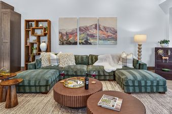 The comfortable living area of Nocturne View features a green sectional sofa, wooden coffee tables, and mountain artwork, with a large window offering views of a snowy landscape.