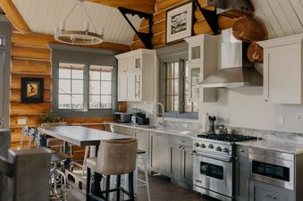 The kitchen at Summit Cabin at See Forever, featuring light gray cabinetry, stainless steel appliances, granite countertops, and a wooden dining table with bar stools.