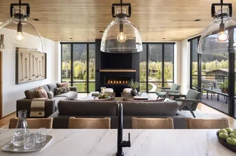 A modern living room in The Sylvan Lodge Two Bedroom Canopy Suite with panoramic mountain views, a cozy fireplace, comfortable seating, and stylish decor, bathed in natural light.