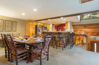 The dining area and kitchen of 88 Ridge Point are beautifully appointed, featuring a large wooden dining table set for a meal, rustic chairs, and a well-equipped kitchen with a breakfast bar.