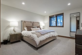 The bedroom in the Antlers Estate features a large bed with a light-colored duvet, multiple pillows, and a patterned throw blanket, flanked by a modern nightstand with a lamp and a tall mirror reflecting the room.