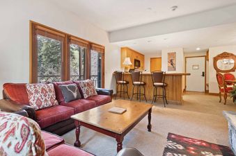 The lounge area in The Charter C0105 features a large red sectional sofa, a wooden coffee table, and a wet bar with stools.