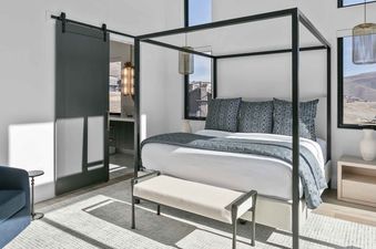A modern bedroom with a black four-poster bed, white linens, and blue accents at Amanti Lago 1757.