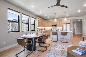The Mayflower Lakeside 204's open-concept living area features a dining table, a modern kitchen with an island, and large windows with an exterior view.
