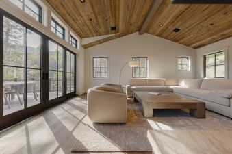 A bright living room with a large sectional sofa, wooden coffee table, and expansive windows looking out onto a mountain landscape.