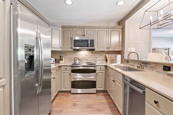 A modern kitchen with stainless steel appliances, light wood flooring, and light brown cabinets.