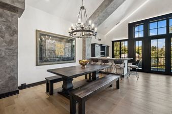 A sophisticated dining area at The Gallatin features a dark wood table with benches, a chandelier, a bar area, and large windows with outdoor views.