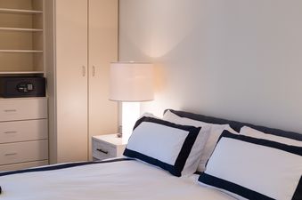 The picture shows a cozy bedroom with a large bed, a nightstand with a lamp, and closet space with a safe.
