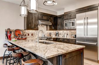 A modern kitchen with stainless steel appliances, dark wood cabinets, and a granite countertop with bar seating.