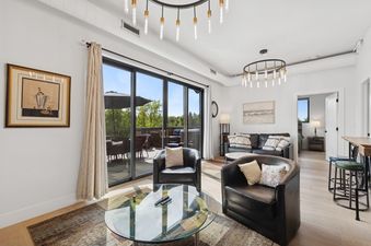 A modern living room with black leather seating, a glass coffee table, and large sliding doors leading to an outdoor patio.