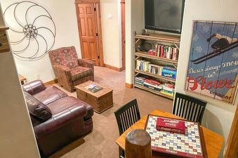 A cozy lounge area at EagleRidge Townhomes 1479 with a leather sofa, armchair, and a Scrabble game set up on a wooden table, with shelves of books and board games nearby.