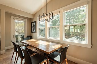 Dining table and chairs under a modern chandelier with large windows showcasing outdoor scenery in Park City Woodside Escape.