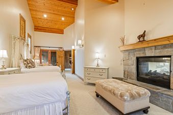 A cozy bedroom at Oak Wood Lodge with two beds, a stone fireplace, and rustic wooden accents.