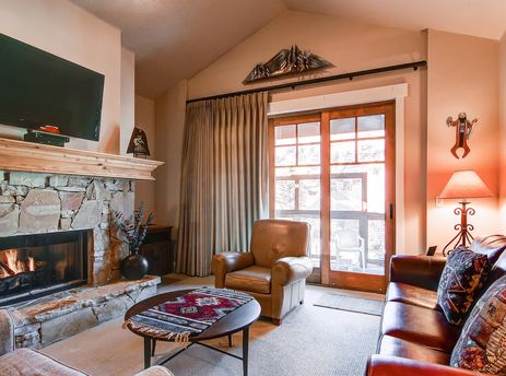 The living room at Town Pointe B303 showcases a cozy fireplace, comfortable leather seating, and a large glass door leading to a balcony.