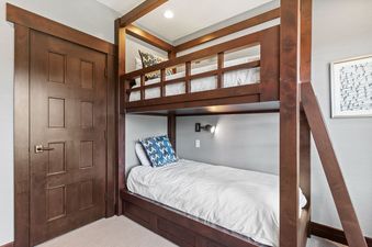 A cozy bedroom in Flagstaff 507 features custom-built dark wood bunk beds with white bedding and blue patterned pillows, alongside a paneled wooden door and light-colored carpet.