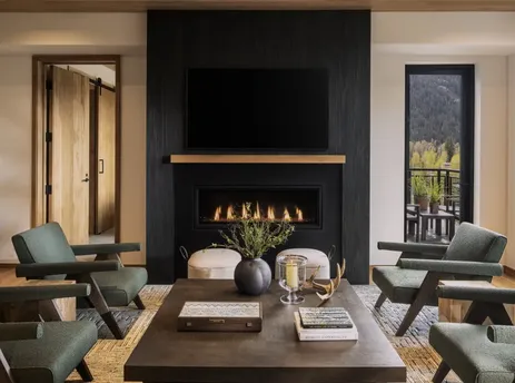 A cozy living area of The Sylvan Lodge Two Bedroom Suite features a fireplace, comfortable seating, and a balcony with an exterior view.