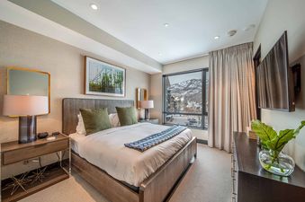 A modern bedroom in One Snowmass Residence Club 407 features a king-sized bed, a large window with mountain views, and sophisticated decor.