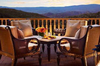 A cozy outdoor seating area with comfortable chairs, a small table with drinks and snacks, and a scenic mountain view at dusk.