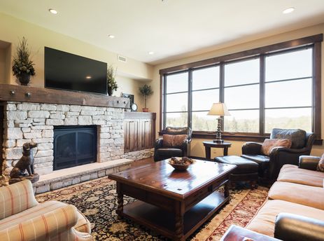 A spacious and inviting living room with a large stone fireplace, plush seating, and a large window offering an exterior view.