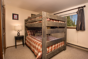 The bedroom in Beaver Village 211 features a sturdy wooden bunk bed with plaid bedding, a bedside table with a lamp, and a window offering a view of lush trees, creating a cozy and rustic atmosphere.