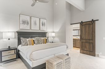 A spacious bedroom in Stonebridge 1158 with a large bed, elegant dark wood furniture, nature-inspired artwork, and a sliding barn door leading to a private bathroom.