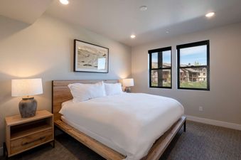 A master bedroom at the Retreat at Jordanelle with a wooden bed frame, white bedding, and large windows looking out onto the property.