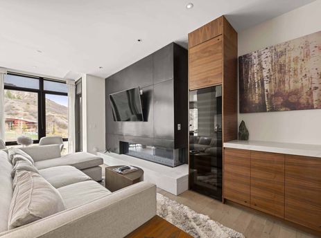 A modern, bright living area in One Snowmass West 301 with a grey sectional, contemporary fireplace, and mountain views.