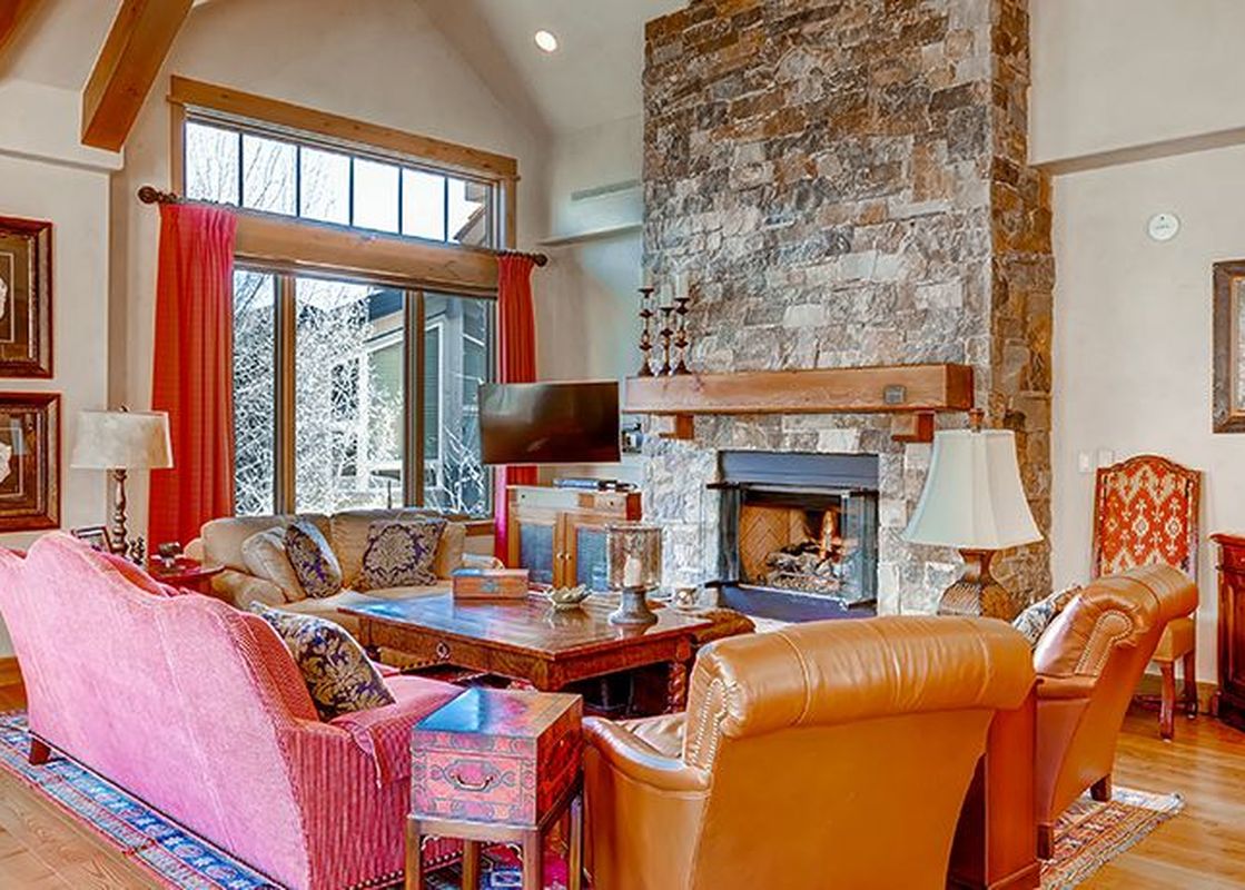 A cozy living room in Arrowhead Village Condominium Platinum 5 Bedroom features a stone fireplace, comfortable seating, and large windows revealing a winter wonderland.