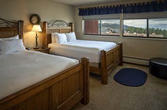 A cozy bedroom in the Two Bedroom Suite Beaver Run Resort with two queen beds, a nightstand with a lamp, and a window offering a mountain view.