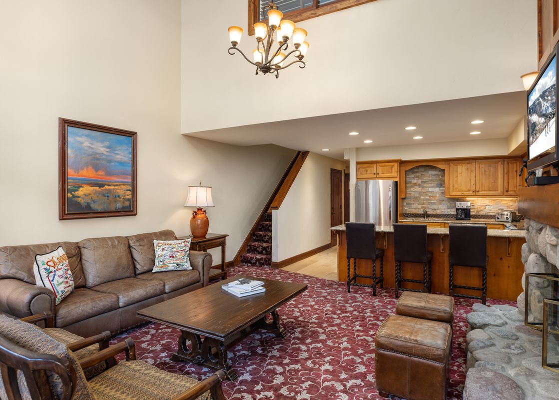A living area with a fireplace, a brown leather sofa, and an open-concept kitchen with a breakfast bar.
