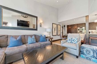 A comfortable living room at The Charter B440 with a grey sectional sofa, blue pillows, a dark wood coffee table, and a large mirror reflecting a television.