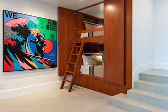 Built-in wooden bunk beds with a ladder in a room next to a vibrant surfing bear painting.
