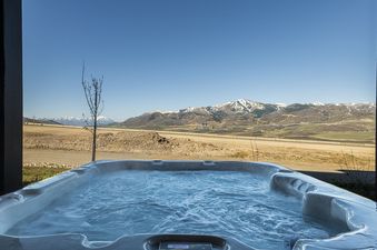 A bubbling outdoor hot tub at Hideout Epic View with a view of snow-capped mountains and a sprawling landscape under a clear blue sky.