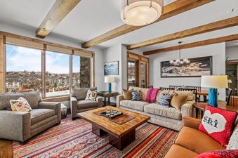 The living room of Edgemont 2401 features a warm and inviting atmosphere with comfortable seating, a rustic coffee table, and large windows offering panoramic views of the snowy mountain town.