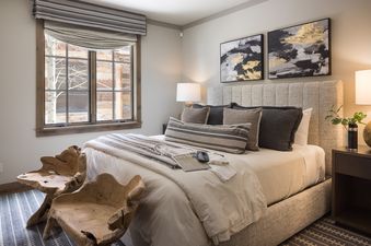 A cozy and stylish bedroom at Fish Creek Lodge 05 with a large bed, unique wooden chairs, and abstract artwork.