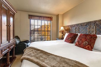 A cozy bedroom in Copperbottom 205 with a large bed, elegant headboard, a wooden armoire, and a window showcasing autumn trees.